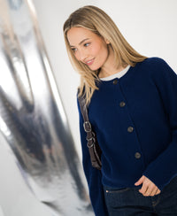 Navy merino wool vest shown from the front, displayed by a model standing next to a shiny metallic surface.