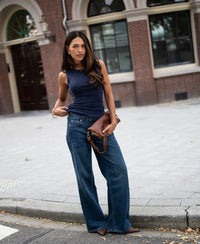 Woman wearing a luxe & soft dark blue LE LYS boatneck top by PLEIN PUBLIQUE, pictured on a city street.