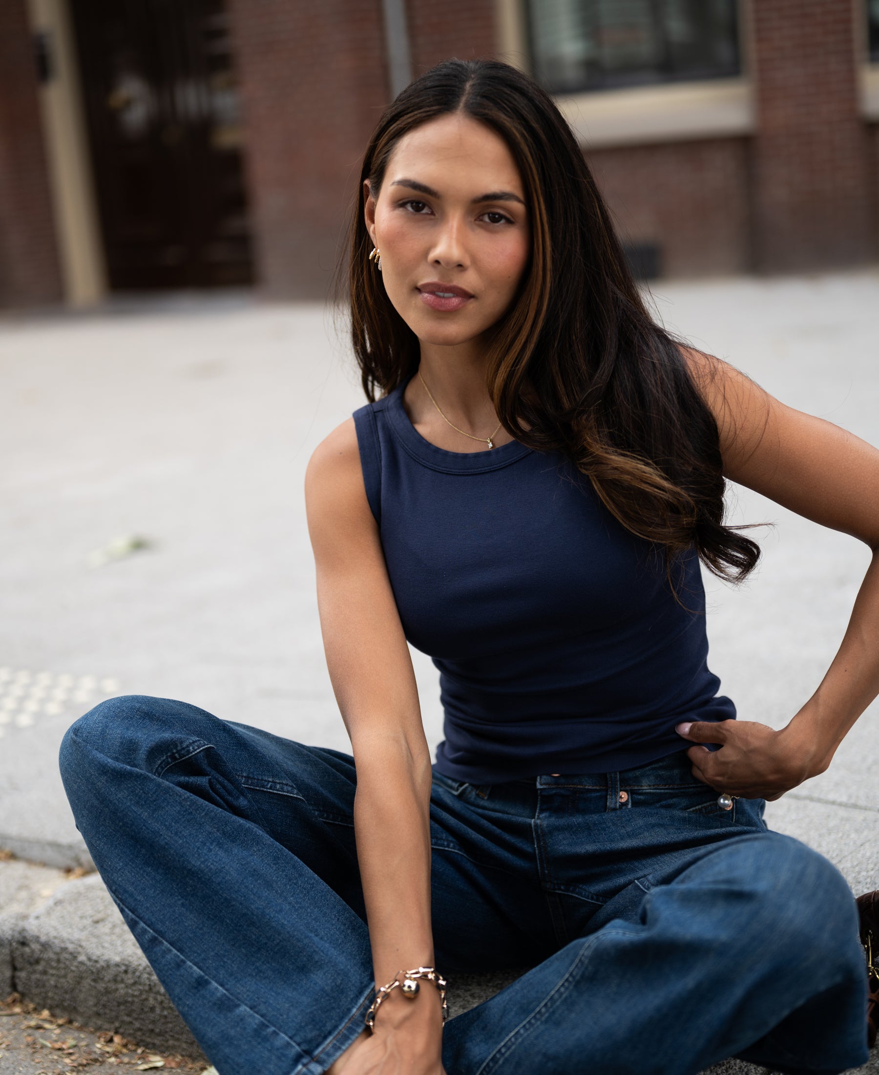 Woman wearing a luxe, soft navy blue boat neck top by PLEIN PUBLIQUE, seated and facing the camera.