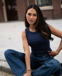 Woman wearing a luxe, soft navy blue boat neck top by PLEIN PUBLIQUE, seated and facing the camera.