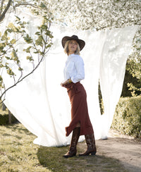 Camel-colored LE MAEL travel skirt from PLEIN PUBLIQUE, shown outdoors by blooming trees.