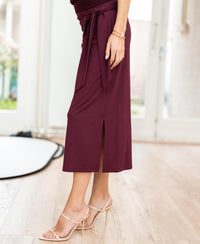 Woman wearing a wine-colored midi skirt with front slit from Plein Publique, shown indoors.