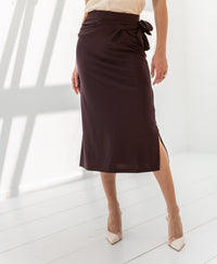 Woman wearing a brown PLEIN PUBLIQUE LE MAEL travel midi skirt in a bright room.