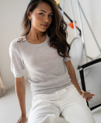 Woman wearing a light grey merino wool sweater, seated indoors.