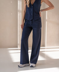 Woman wears PLEIN PUBLIQUE pinstripe trousers LE MALO in dark blue in a sunlit room.