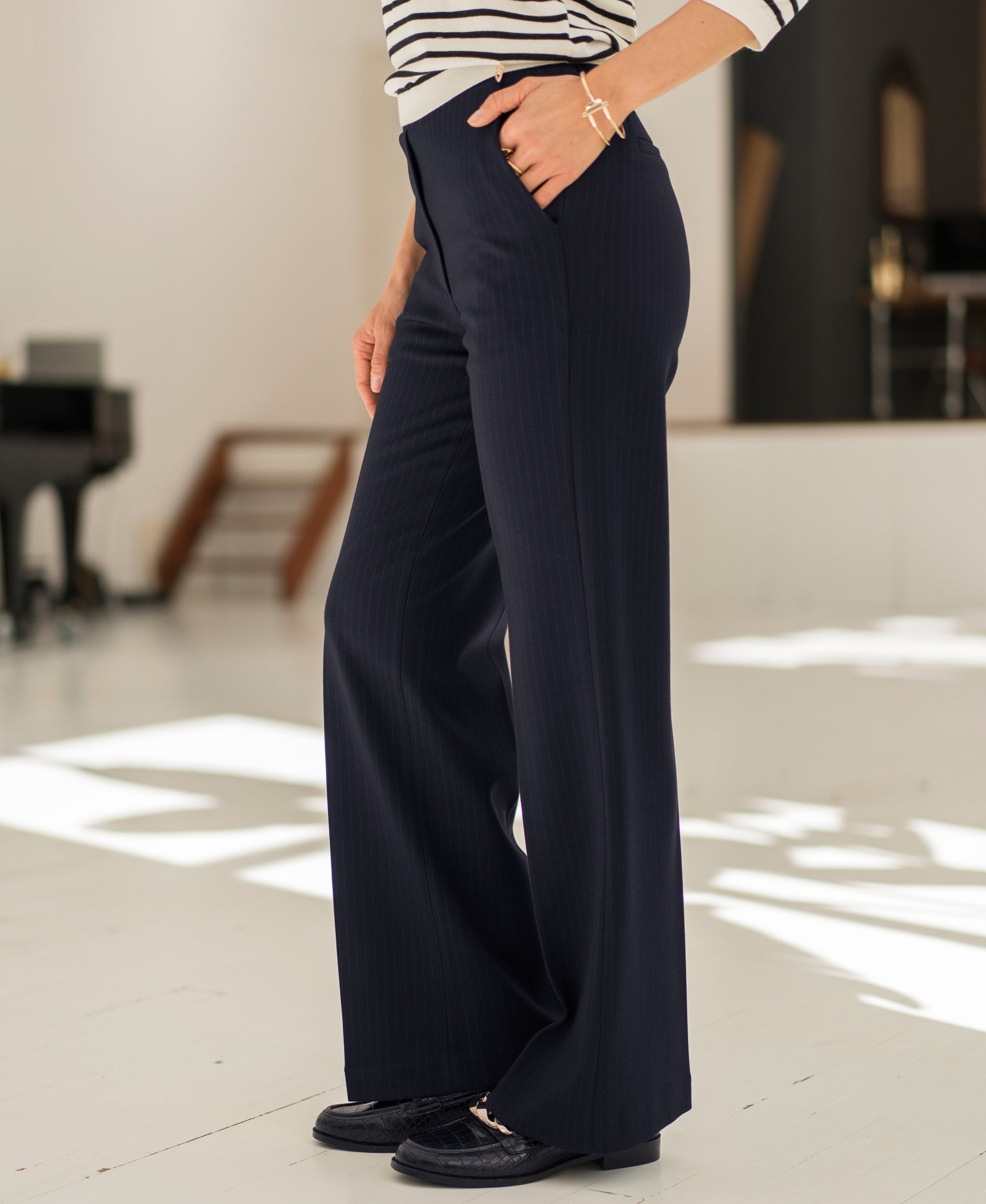 Person wears dark blue pinstripe trousers, hands in pockets.
