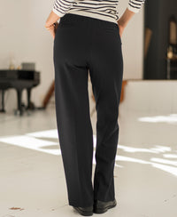 Person wearing black pinstripe trousers stands indoors with their back to the camera.