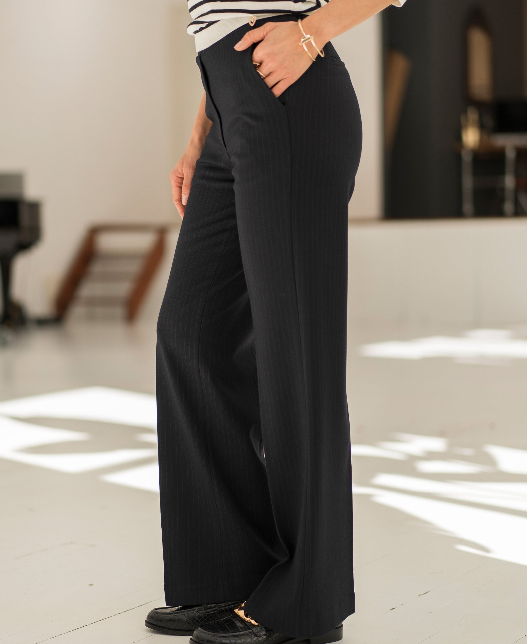 Black pinstripe LE MALO trousers by PLEIN PUBLIQUE, shown with hands in pockets, indoor setting.