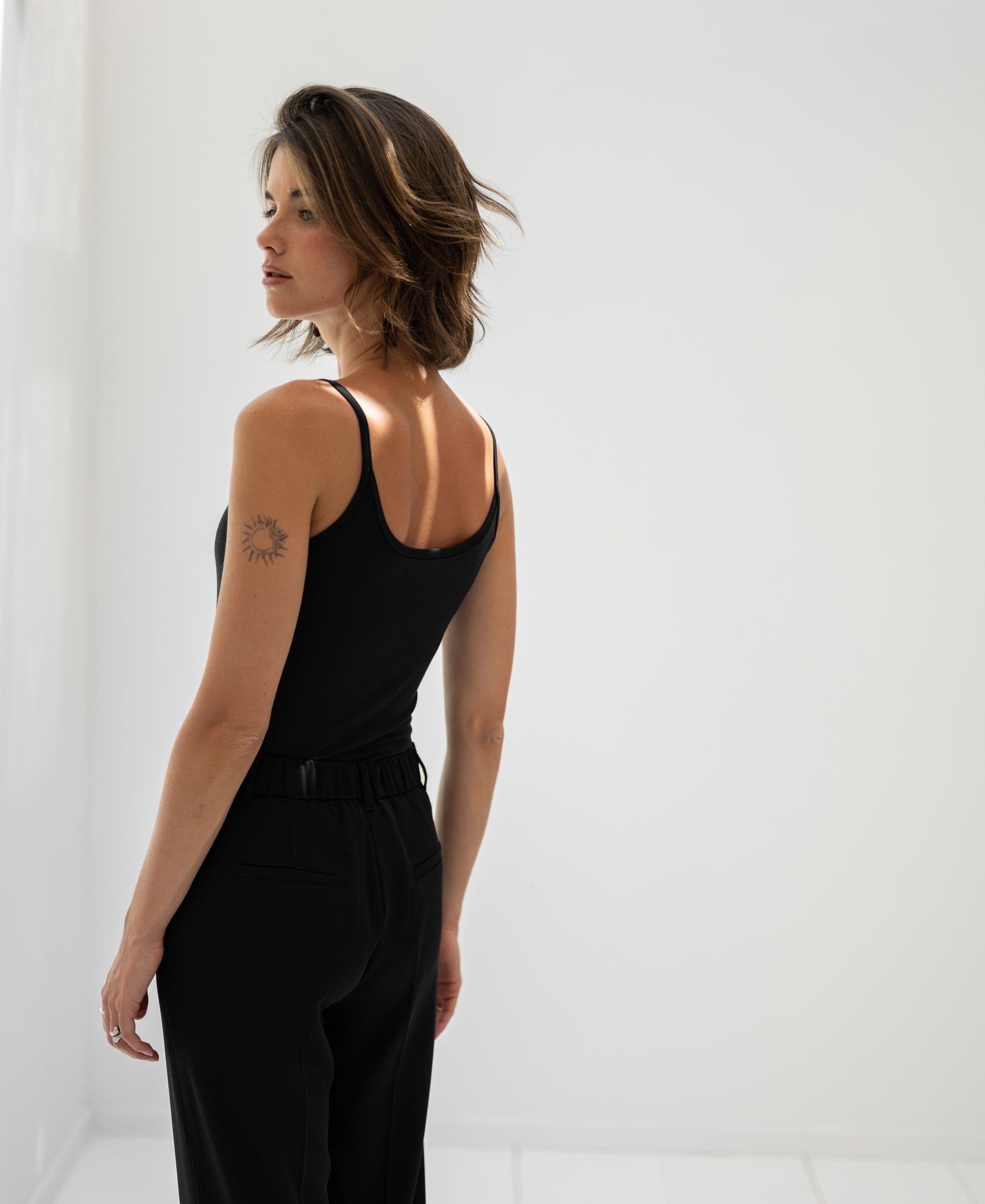Woman wearing black Second Skin Top by PLEIN PUBLIQUE, shown from the side.