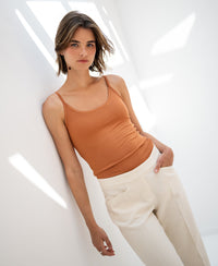 Woman wearing a bright terra Second Skin Top by Plein Publique leans against a white wall.