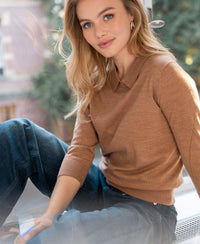 Merino wool polo sweater in Chai Tea color, shown by a woman with long blonde hair standing by a window.