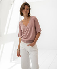 Woman wearing the PLEIN PUBLIQUE silk blend LE MARDY top in dusty rose in a bright, sunlit room.