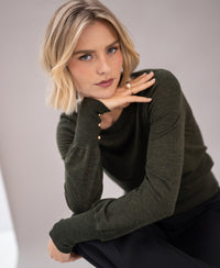 A woman wearing a PLEIN PUBLIQUE Merino wool sweater LA MARIS in dark green-gold.