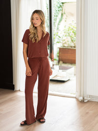 Silky henna lounge pants with a glossy finish, shown indoors by a window as the fabric catches the light.