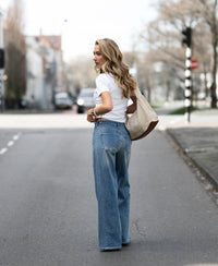 Woman wearing wide leg light stone wash jeans stands on the street, looking back.