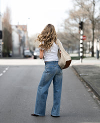 Wide leg jeans in light stone wash, shown from the back as the model stands facing away in an empty street.