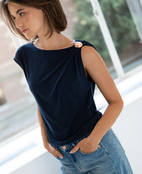 Woman wearing the LA MAYA dark blue top with buckle by PLEIN PUBLIQUE, standing indoors near a window.