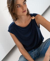 Navy blue LA MAYA top with buckle detail from PLEIN PUBLIQUE, shown on a woman sitting on the floor, side view.