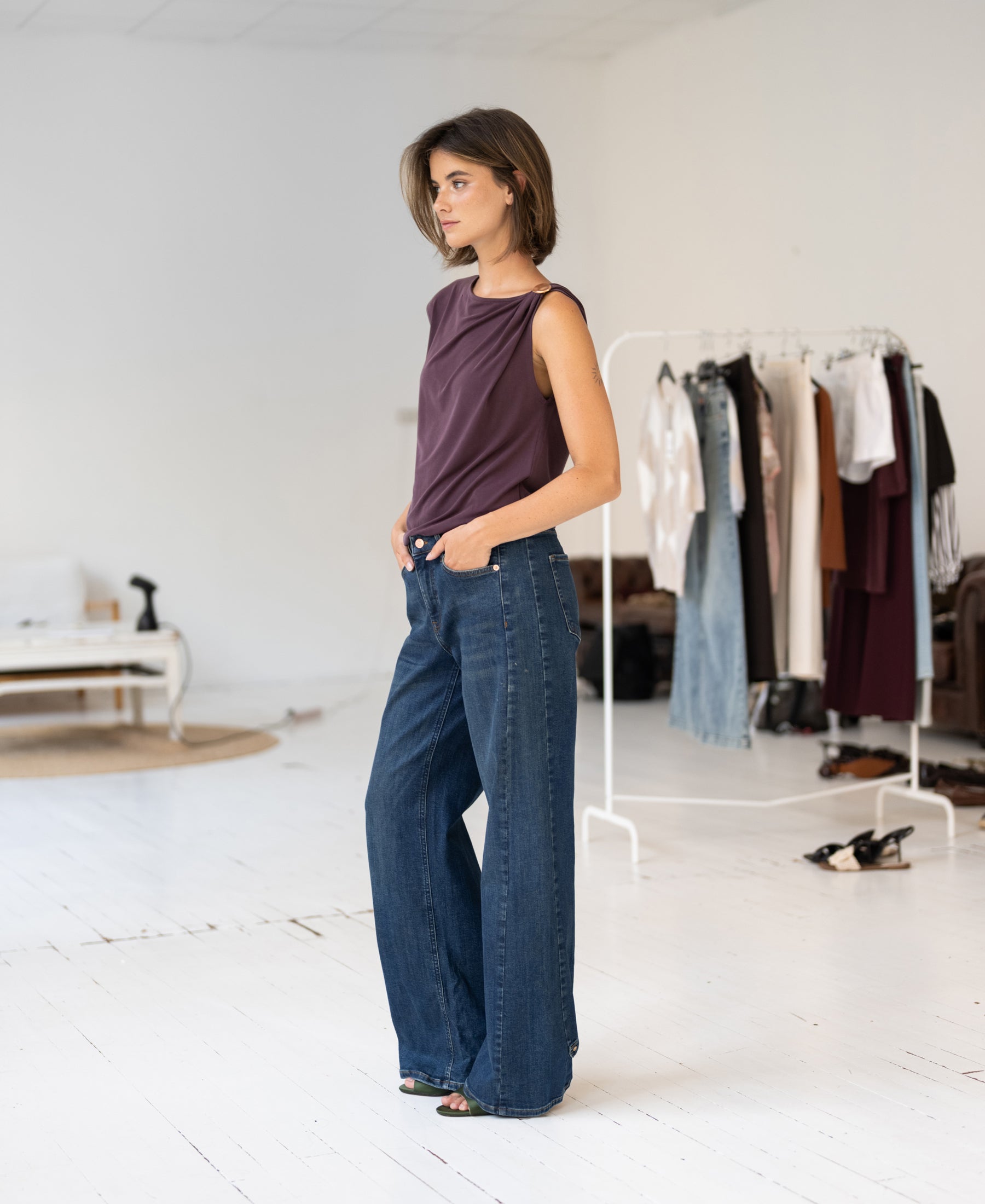 Blue heritage wide leg jeans in a bright room, shown full-length on a person standing by a clothing rack.