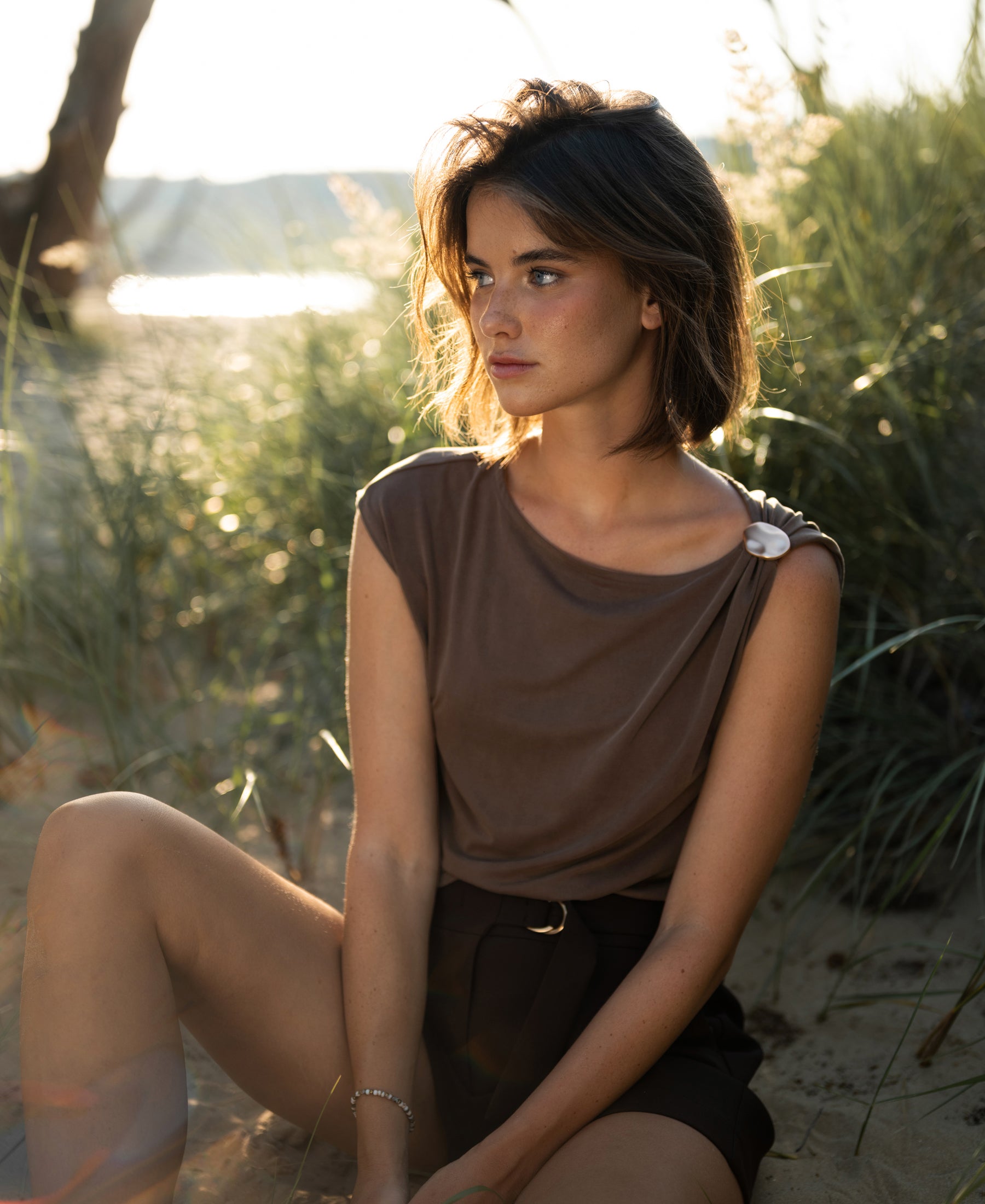 Brown LA MAYA top with buckle detail from PLEIN PUBLIQUE shown outdoors.