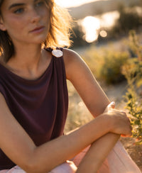 Wine-colored Plein Publique LA MAYA top with buckle detail, shown outdoors with greenery and soft sunlight in the background.