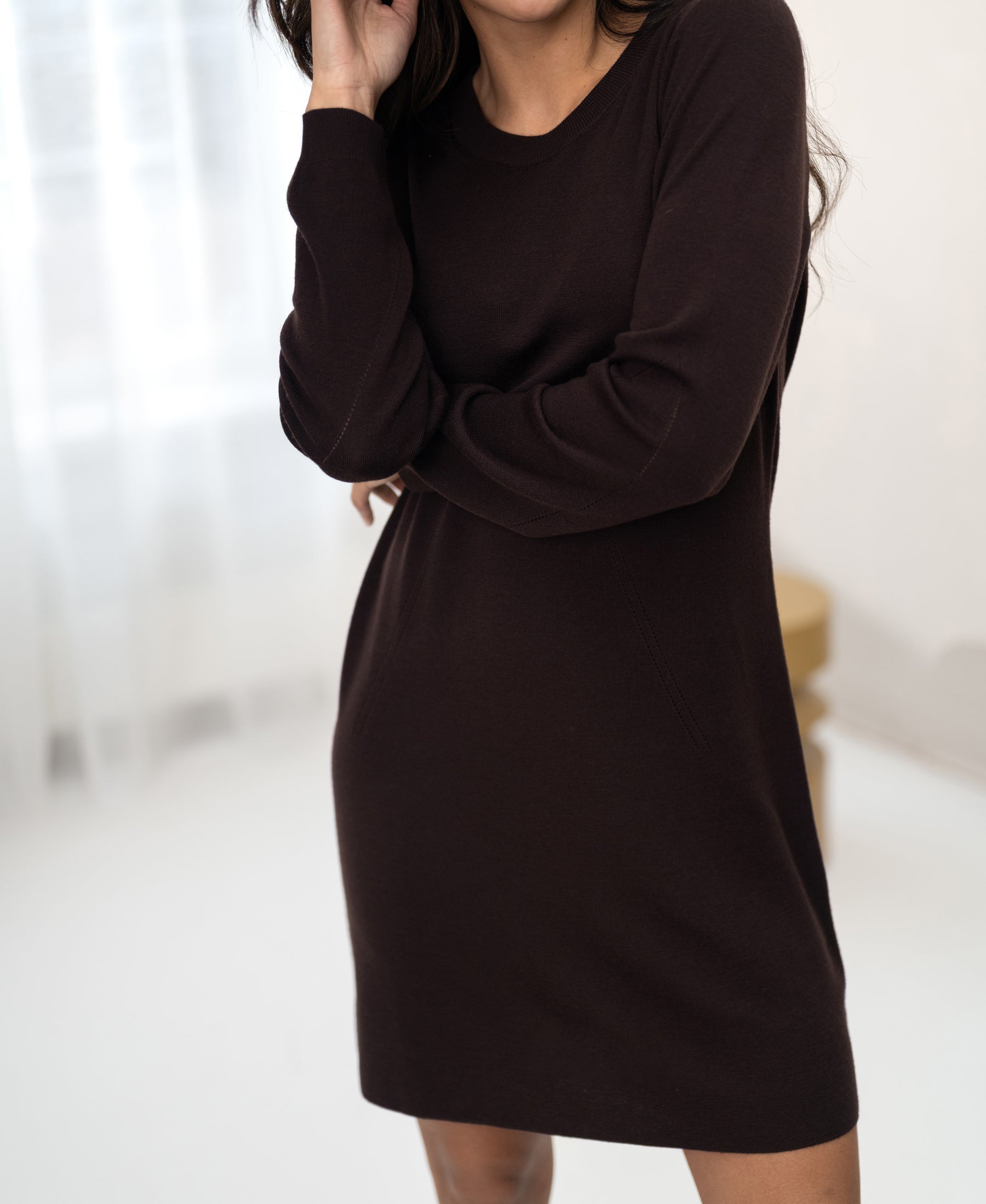 Brown merino wool LA MIMI dress by PLEIN PUBLIQUE shown indoors by sheer white curtains.