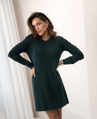 Dark green merino wool dress by PLEIN PUBLIQUE, shown indoors on a model standing with hands on hips.