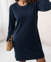 Woman wearing a denim blue LA MIMI merino wool dress by PLEIN PUBLIQUE indoors against a light background.