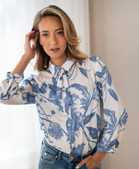 Woman wearing floral print blouse with tie detail, LA MINOU brand, size XL, indoors.