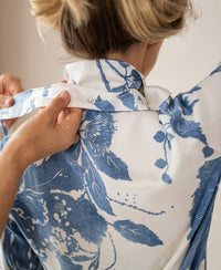 Person fastening a blouse with tie detail and floral print.
