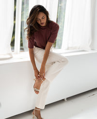 Woman wearing a ribbed cacao-colored top from PLEIN PUBLIQUE, sitting on a windowsill.