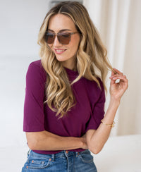 Woman wearing a magenta ribbed collared top.