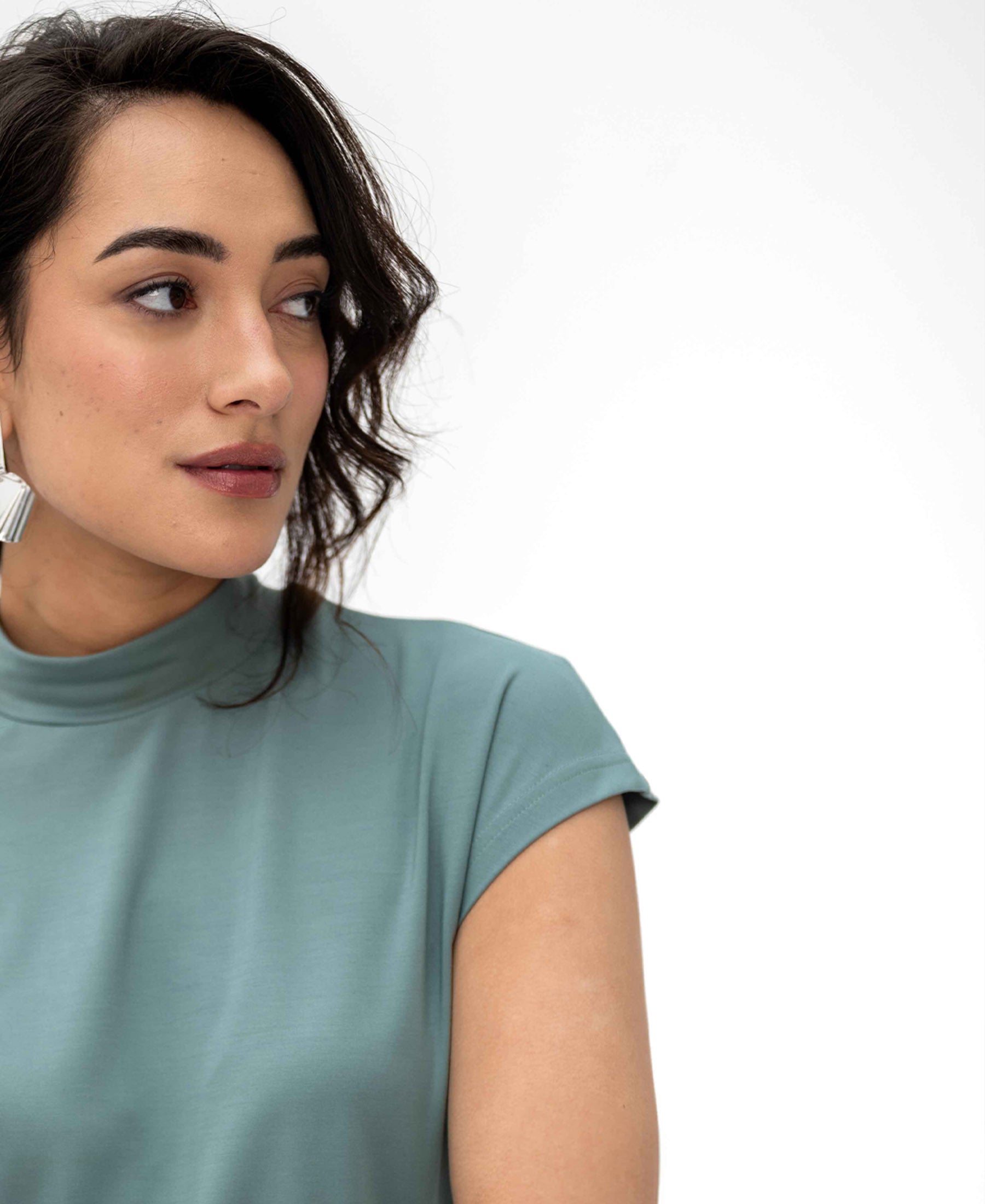 Woman wearing PLEIN PUBLIQUE’s light green LA ROMY travel top, shown from the side against a white background.