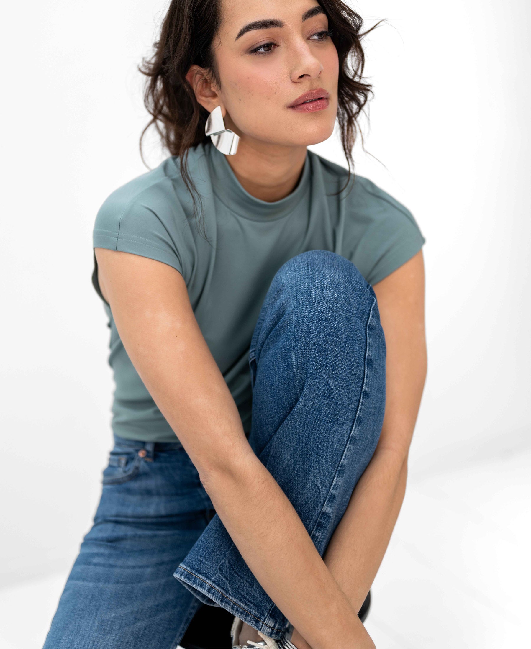 Woman wearing a PLEIN PUBLIQUE Travel top in light green (Mistgroen), seated with one knee up.