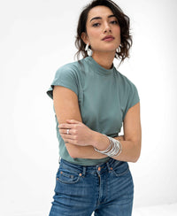 Woman wearing a light green LA ROMY travel top by PLEIN PUBLIQUE on a white background.