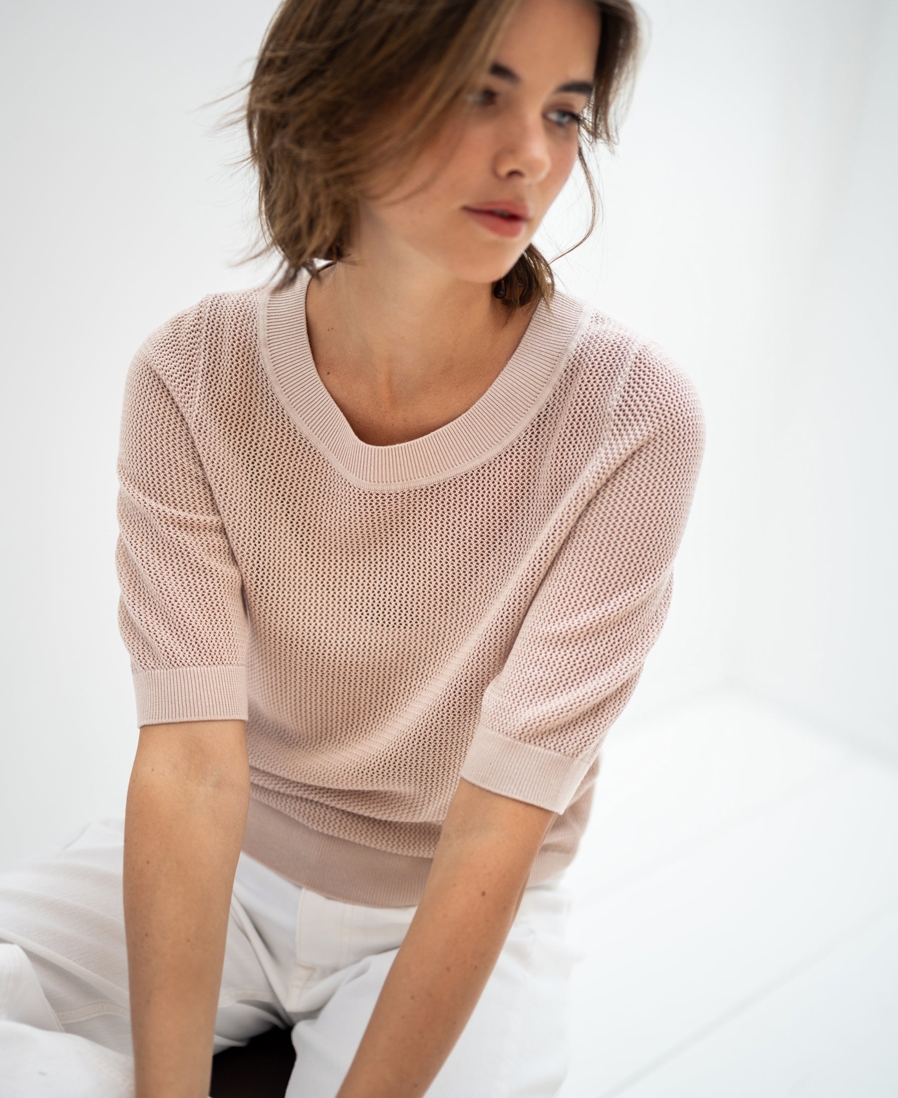 Woman wearing the PLEIN PUBLIQUE mesh sweater LE NANCY with silk in light sand color in a bright, minimal space.