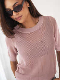 Woman wearing dusty pink mesh sweater with silk, straight brown hair visible, looking down.