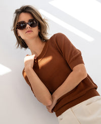 Woman wearing mesh sweater LE NANCY with silk in Havana color stands by a sunlit white wall.