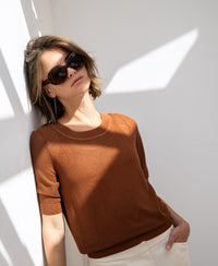 Mesh sweater LE NANCY with silk in Havana by PLEIN PUBLIQUE, worn by a woman leaning against a sunlit wall.