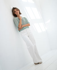 Mist green mesh sweater with silk by PLEIN PUBLIQUE, shown on a woman leaning against a sunlit wall.