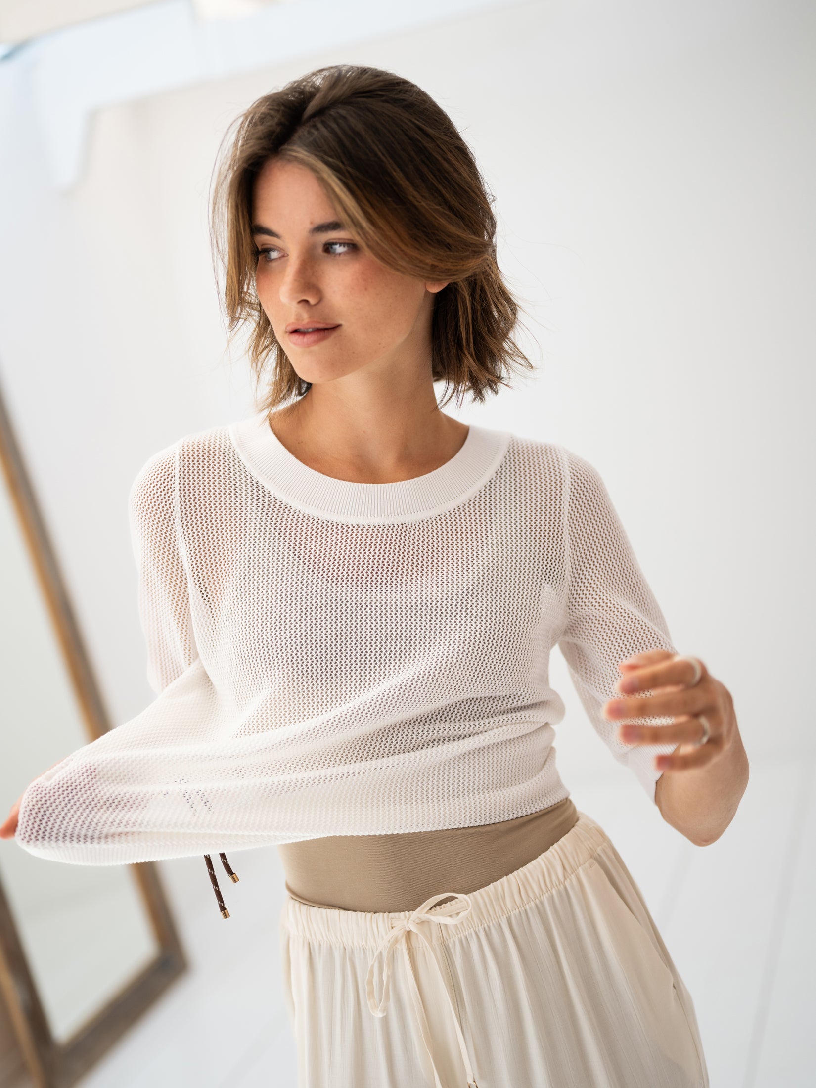 White mesh sweater with silk, shown on a woman in a bright room, side view.