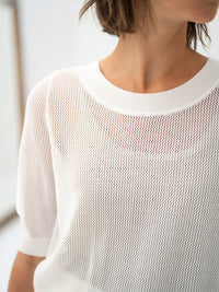 The white mesh sweater with silk by PLEIN PUBLIQUE, shown on the lower face, neck, and torso of a woman.