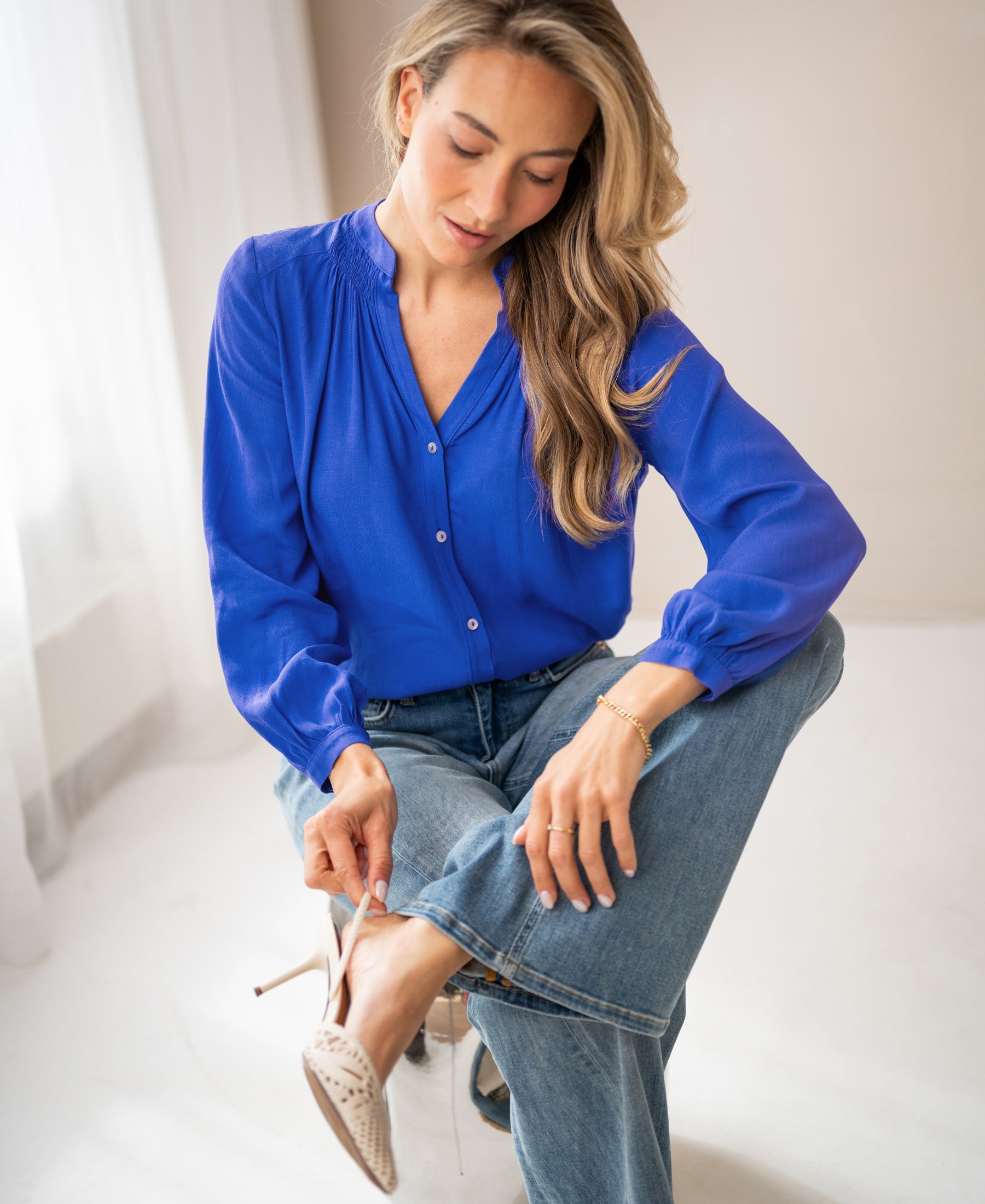 Woman wearing the PLEIN PUBLIQUE LA NIMES Blue Iris blouse in a softly lit room.