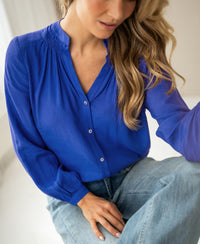 Blue iris blouse in a relaxed fit from Plein Publique, shown worn by a woman with long wavy blonde hair, indoors.