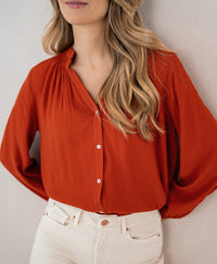 Burned orange blouse with long sleeves from PLEIN PUBLIQUE, shown against a light wall.
