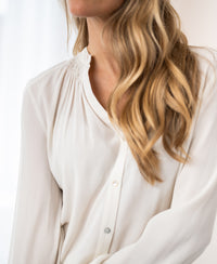 Ivory long-sleeve blouse in a wavy fabric, shown from shoulders down.