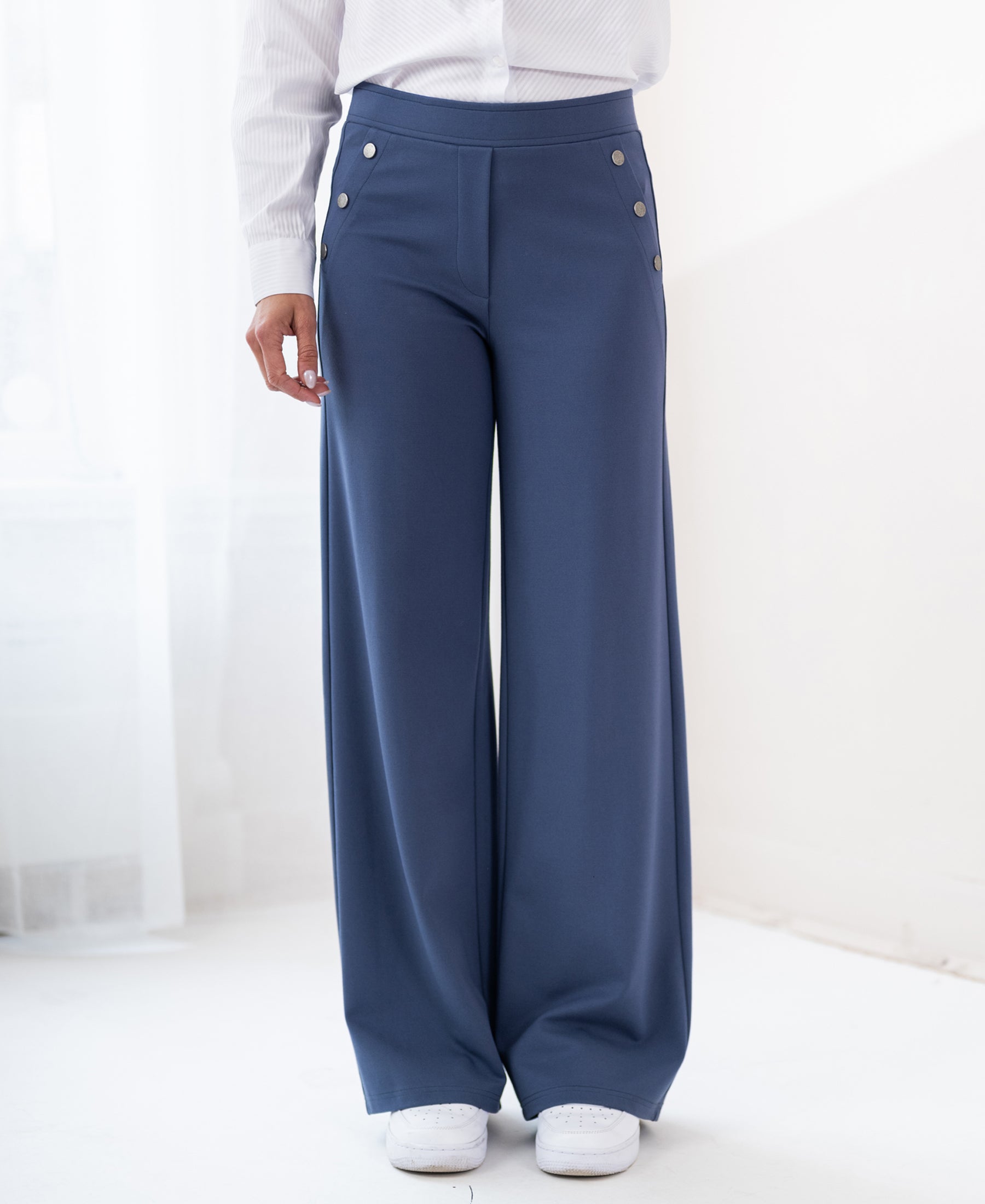 Travel pants LA NOAN Deluxe in blue by PLEIN PUBLIQUE, shown in a sunlit room.
