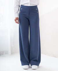 Travel pants LA NOAN Deluxe in blue by PLEIN PUBLIQUE, shown in a sunlit room.