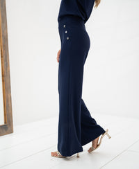 Side view of dark blue travel pants on a woman, shown on a white floor.