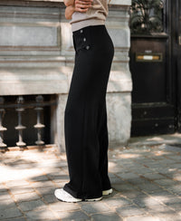 Person outdoors wearing black PLEIN PUBLIQUE LA NOAN Deluxe travel pants, facing sideways.